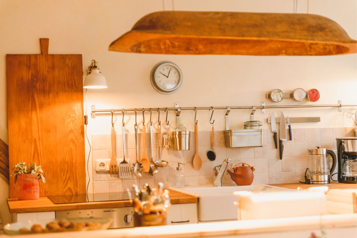 Fliesenspiegel der Küche mit vielen Kochutensielien wie Kochlöffel, Kellen und Bürsten. Links ein großes Schneidbrett.