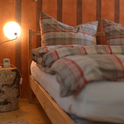 Doppelbett, mit einem Holzstamm als Beistelltisch und einer Orangenen Wand