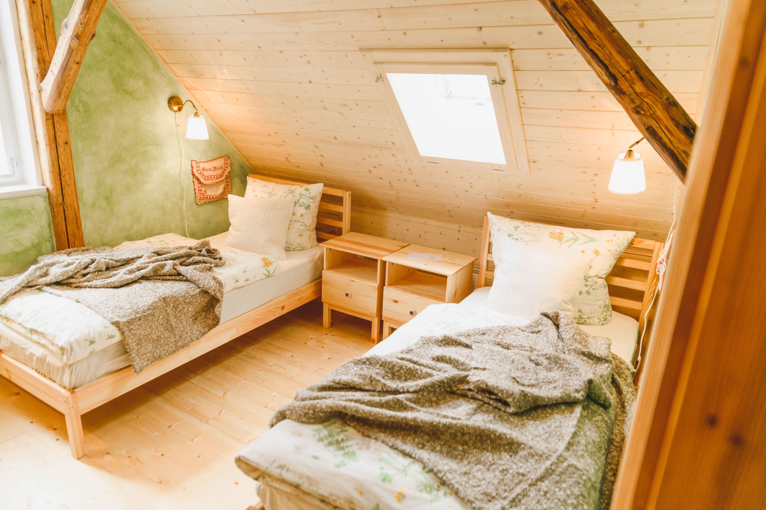 Grün gestrichenes Schlafzimmer mit zwei Einzelbetten, Dachschrägen und Holzbalken. Lampe über jedem Bett.