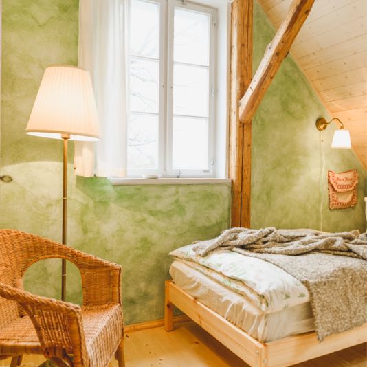 Grün gestrichenes Schlafzimmer mit Einzelbett, Stehlampe und Korbstuhl.