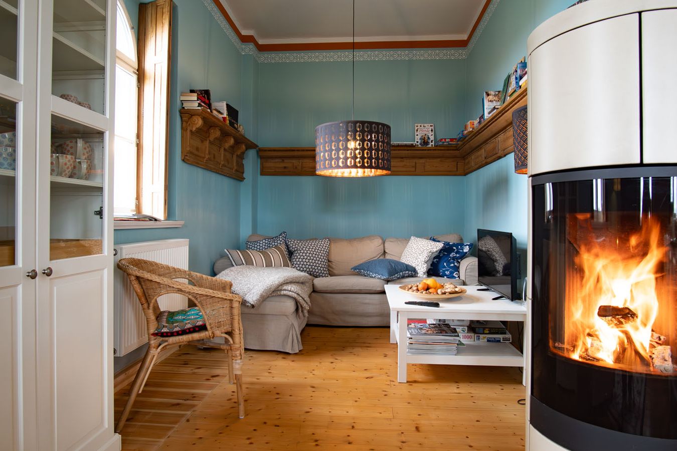 Fernsehecke in blau gestrichenem Zimmer mit Ecksofa, Kamin und Fernseher.