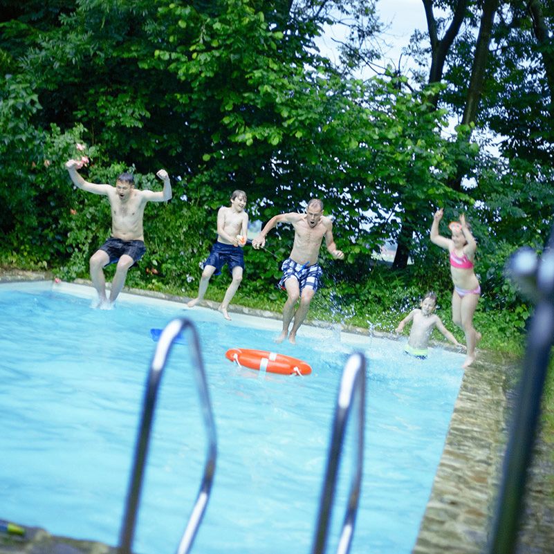 Fünf Personen springen im Garten in einen großen Pool