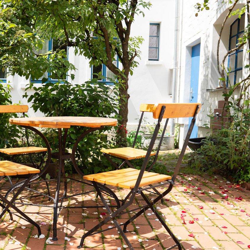 Terrasse im Innenhof mit Tisch und vier Stühlen, rund herum Bäume und Sträucher