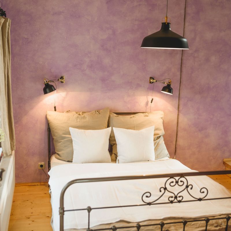 Einblick in ein Schlafzimmer, zu sehen ein Doppelbett an einer violetten Wand
