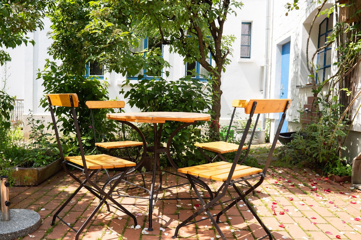 Terrasse im Innenhof mit Tisch und vier Stühlen, rund herum Bäume und Sträucher