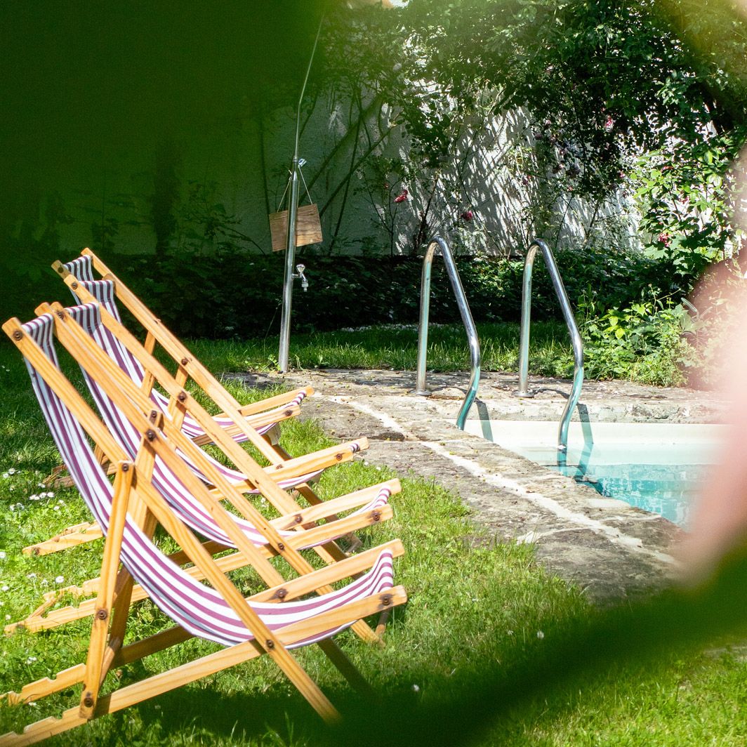 drei gestreifte Liegestühle am Pool, im Vordergrund unscharfe Rosenblüte