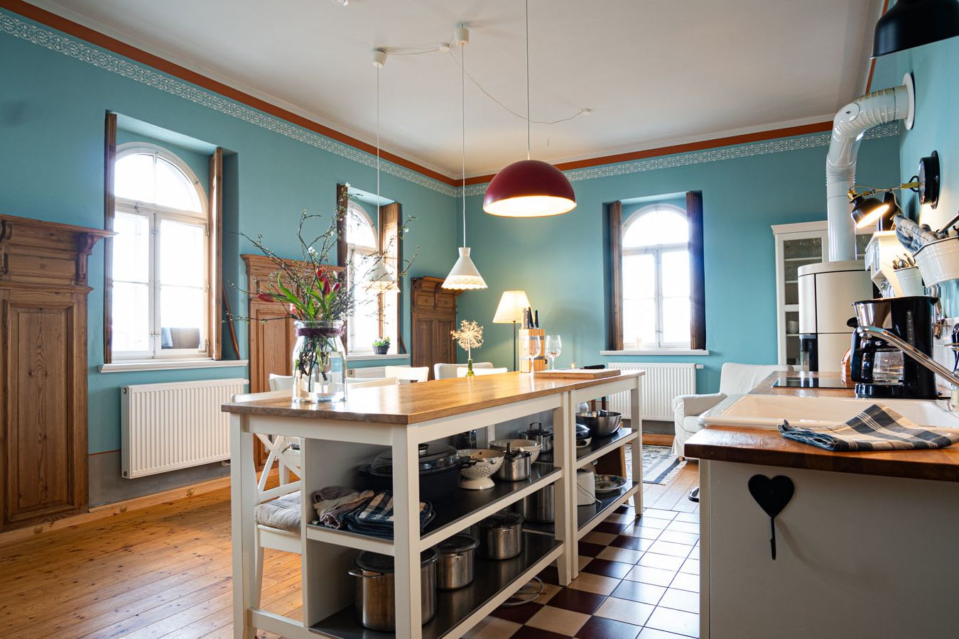 große, blau gestrichene Wohnküche mit Kücheninsel und Fenstern an zwei Seiten