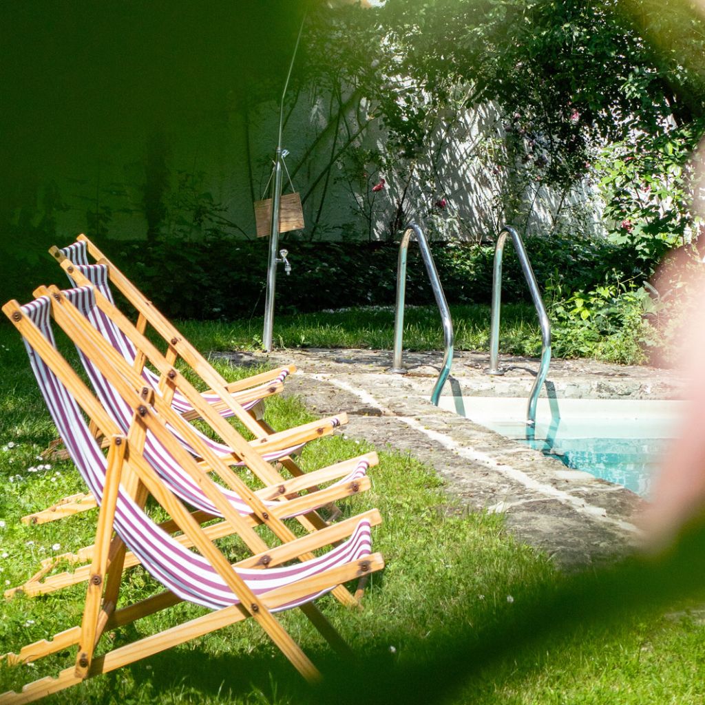 drei gestreifte Liegestühle am Pool, im Vordergrund unscharfe Rosenblüte