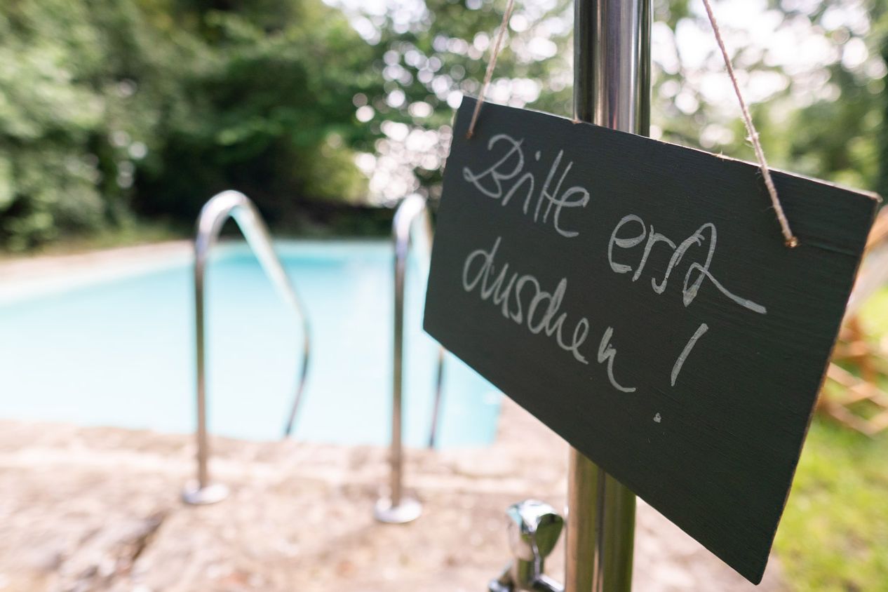 Pool im Grünen, im Vordergrund Schild mit Aufschrift "Bitte erst duschen!"